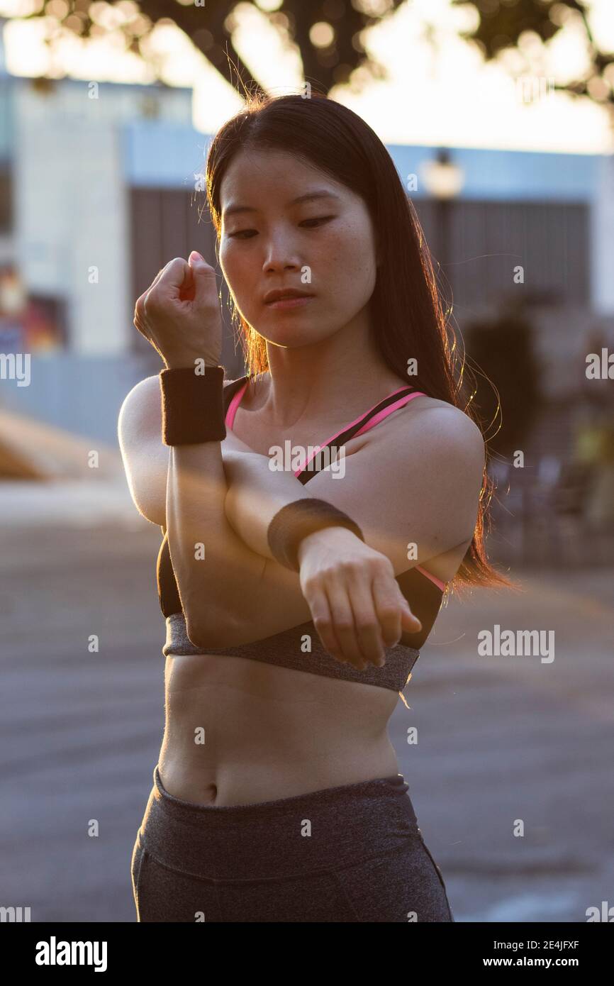 Woman in sports clothing stretching at park during sunset Stock Photo