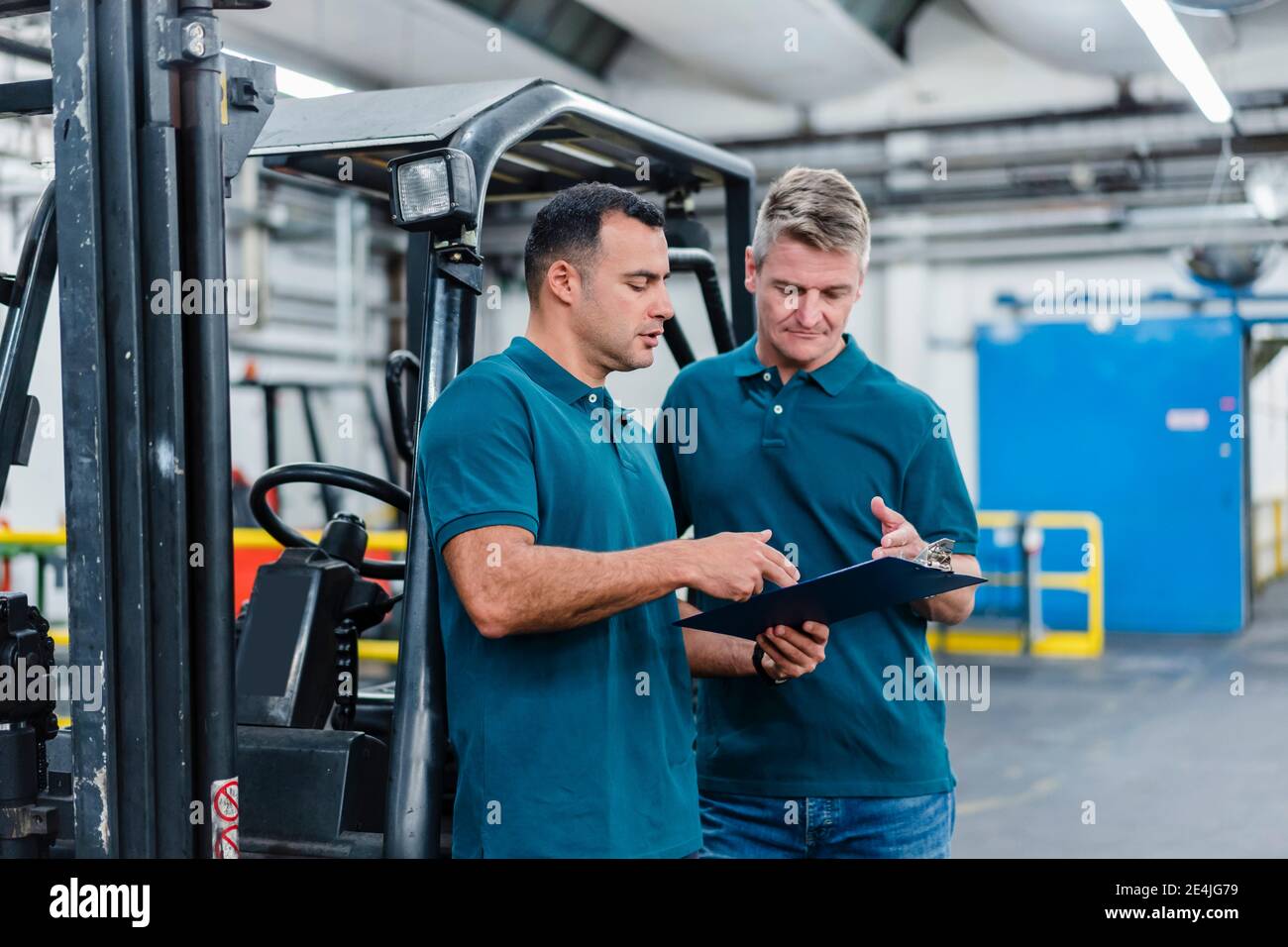 Male colleagues discussing over document while working in factory Stock Photo