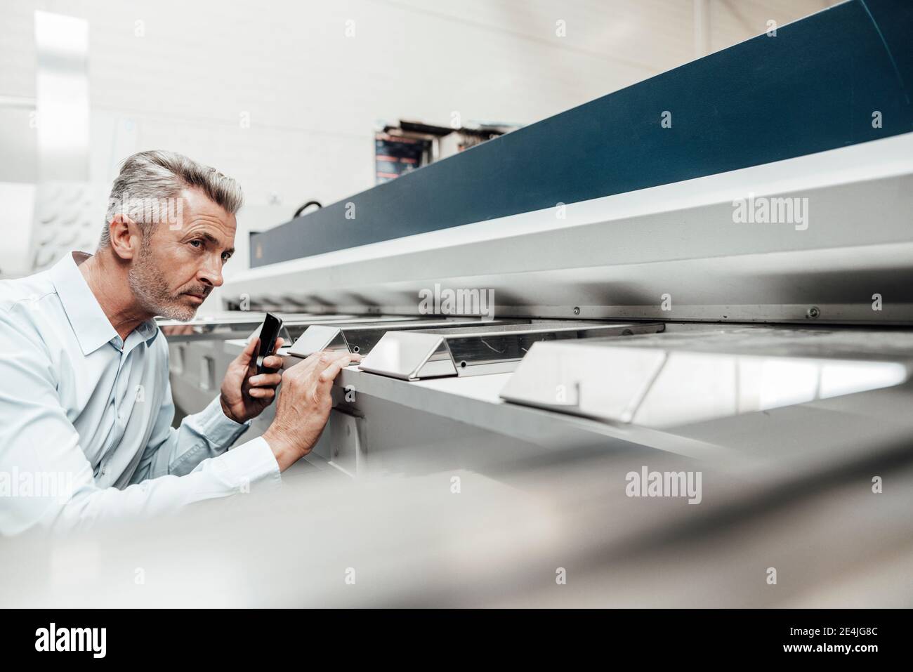 Mature inspector examining machine while standing at industry Stock ...
