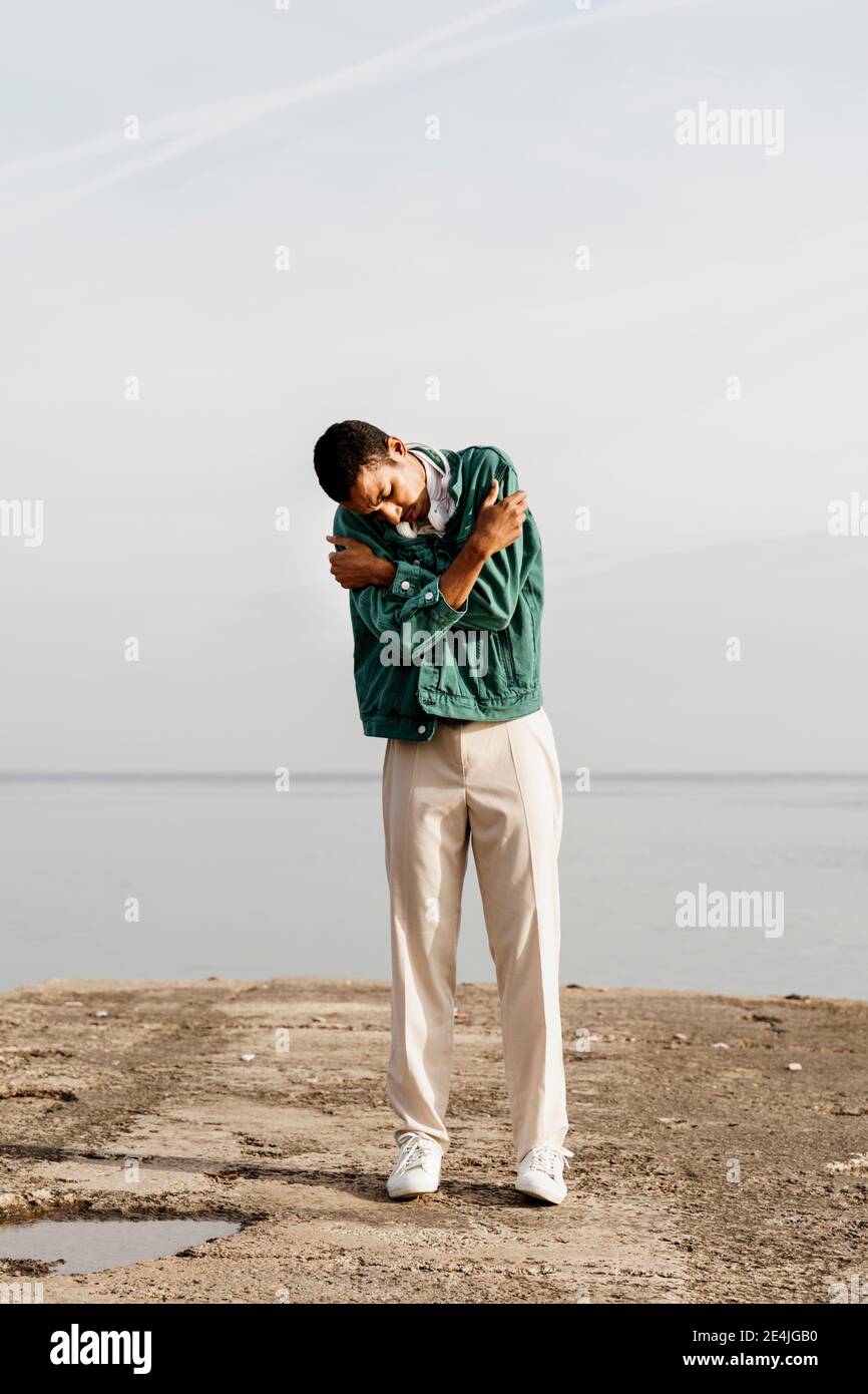 Young man self hugging against sky and sea Stock Photo