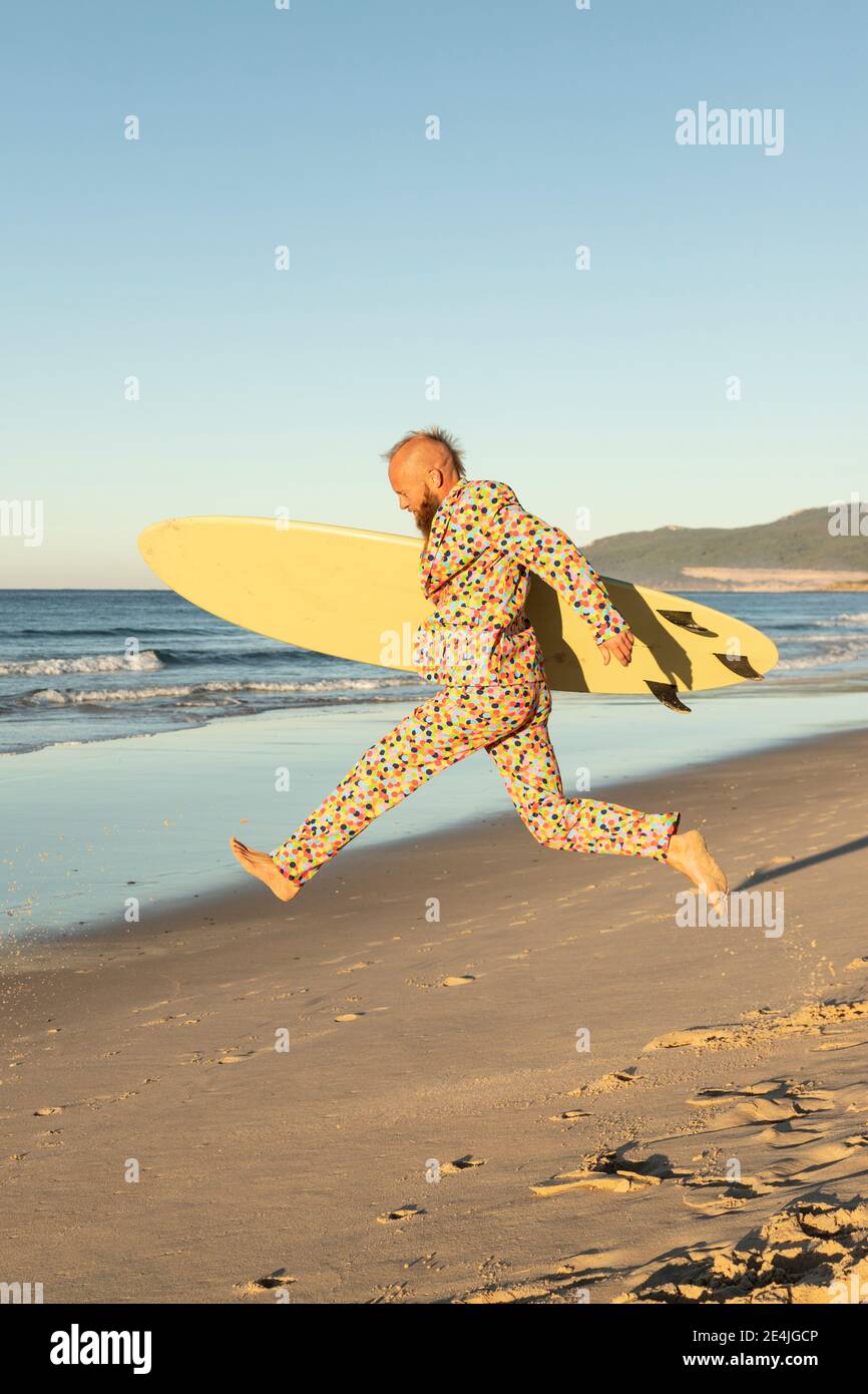 Carefree man running with surfboard on beach Stock Photo