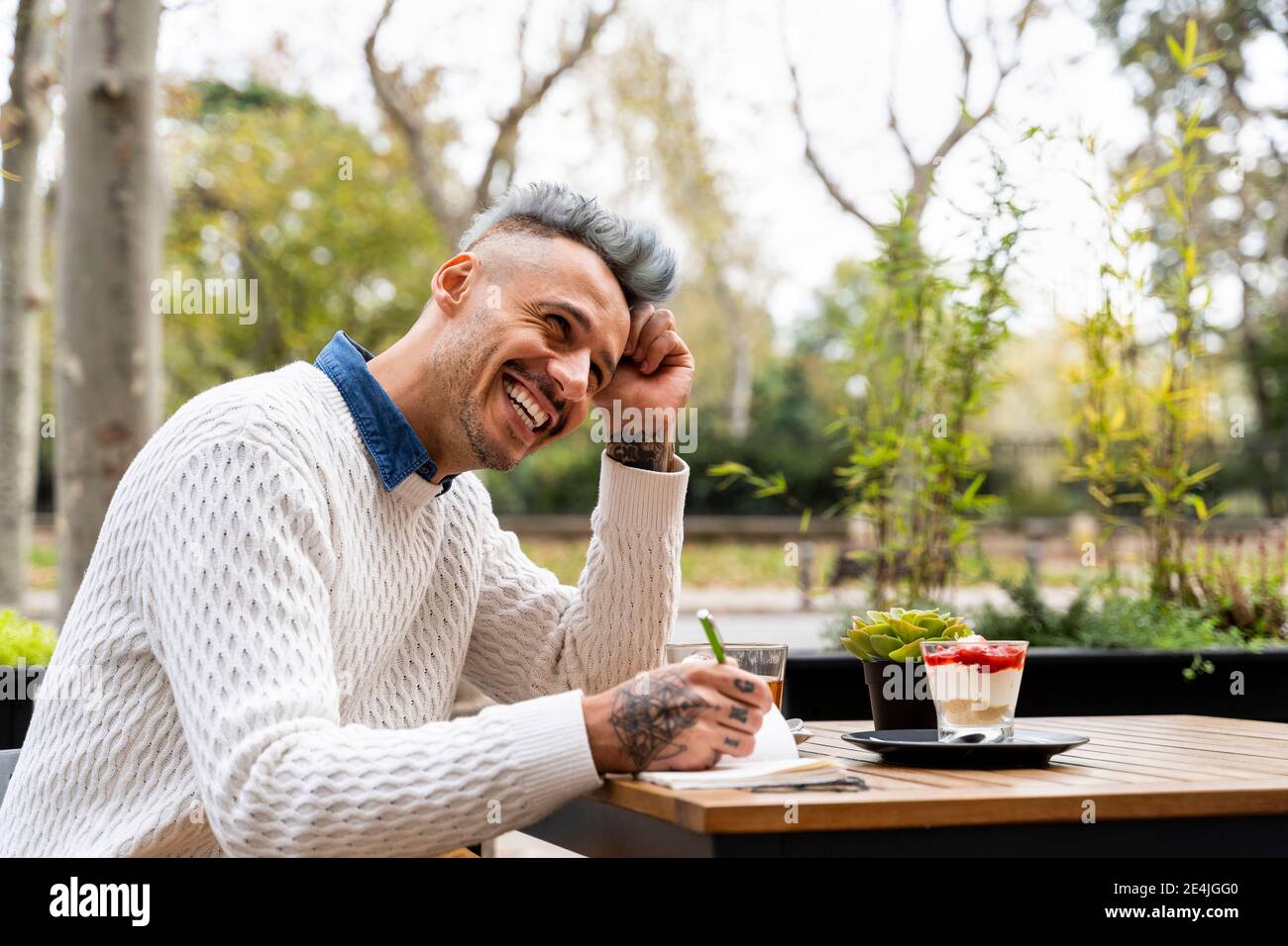 Man laughing while writing in book at sidewalk cafe Stock Photo