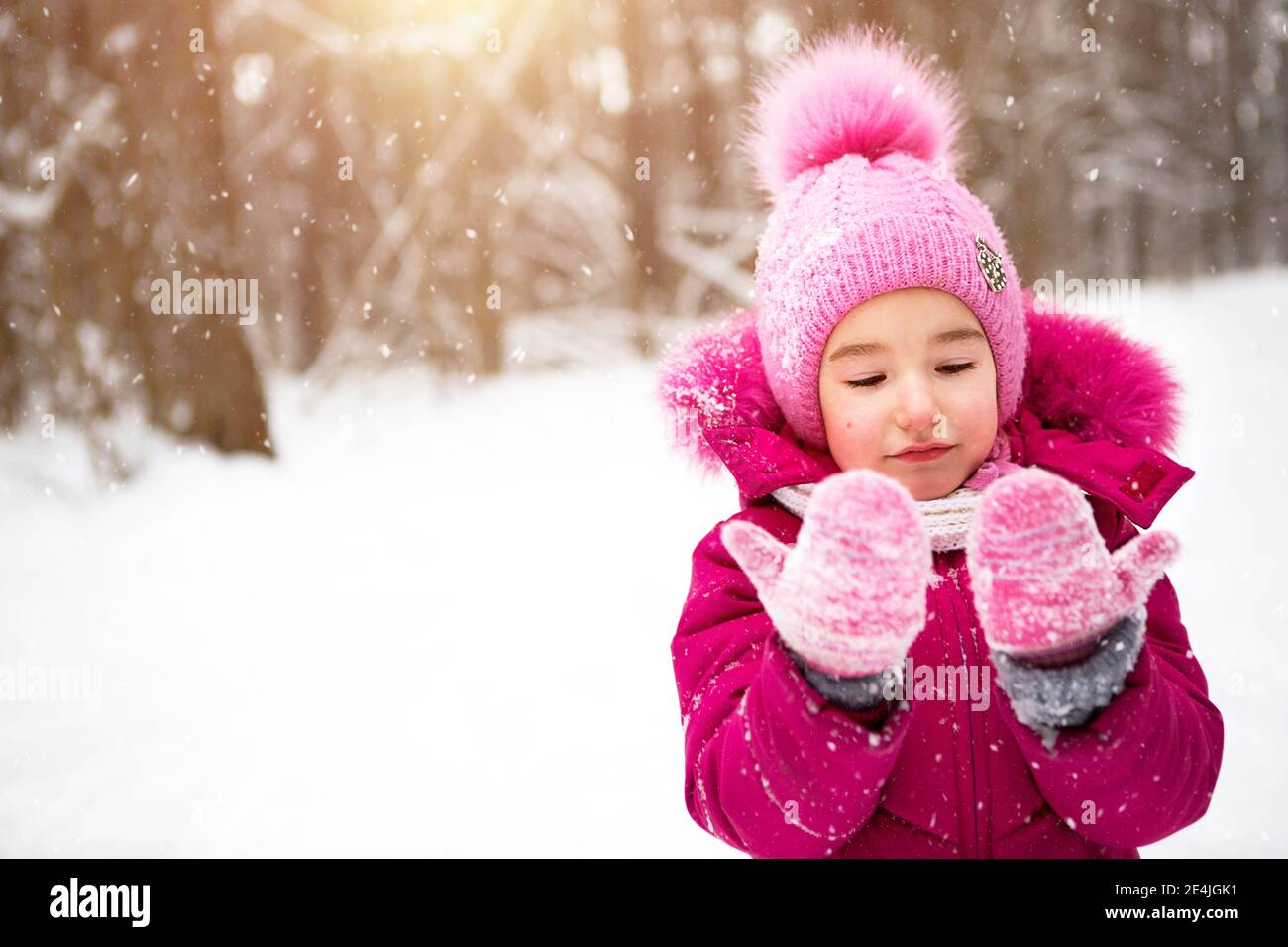Little girl in the cold looks at the snow mittens and smiles. Winter walk the baby in the open air snow. Warm clothing knitted hat fur pompom and Stock Photo Alamy