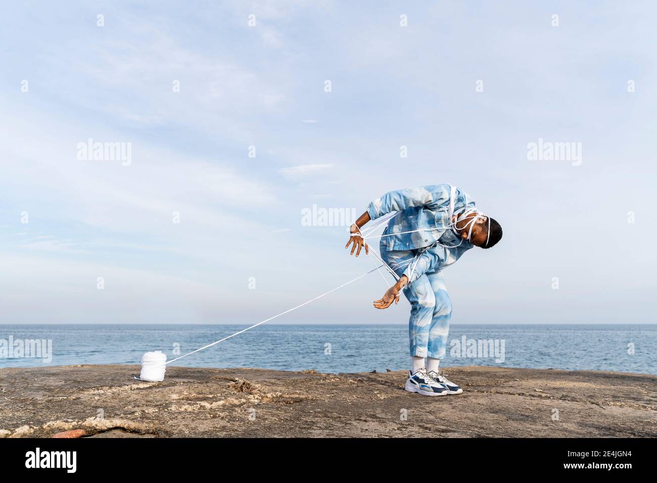 Young man trapped in rope escaping while standing against sky Stock Photo