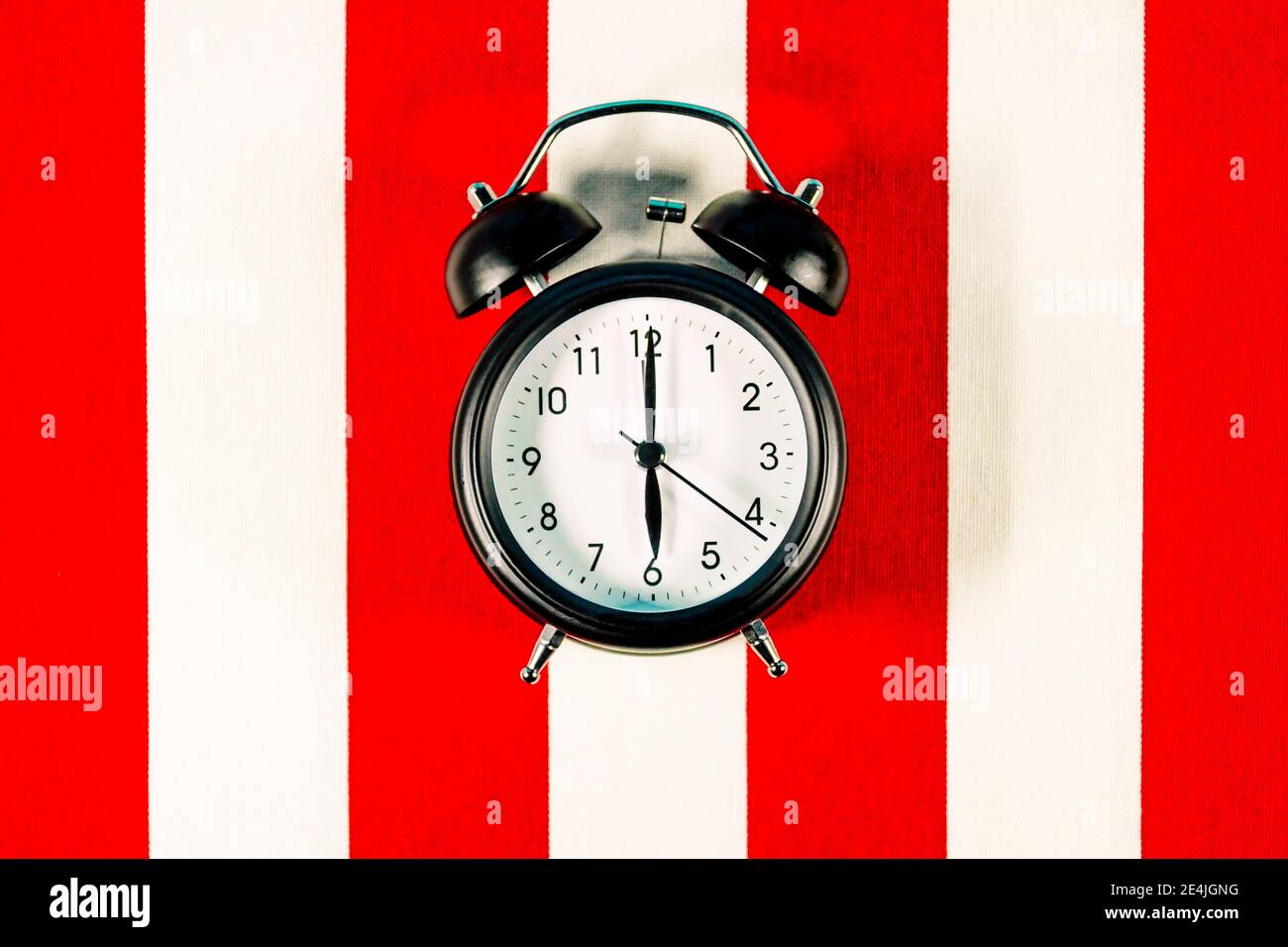 Alarm clock lying on white and red striped pattern Stock Photo