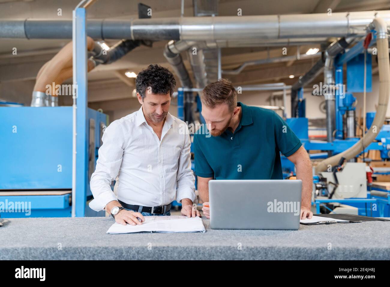Two carpenters talking over documents in production hall Stock Photo