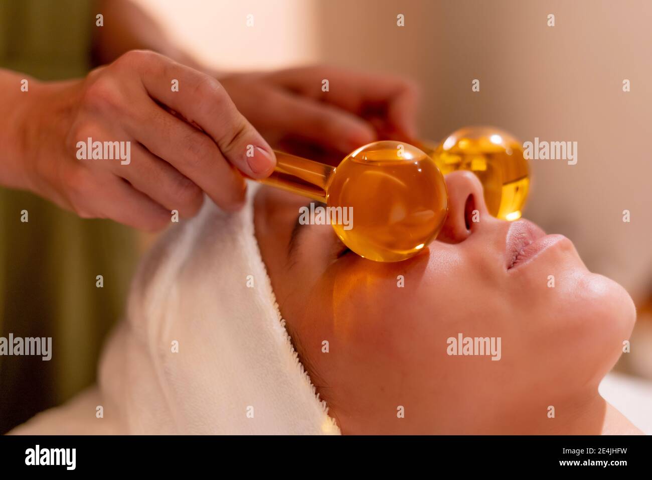 Beautician holding glass globes on female customer's face during spa treatment Stock Photo