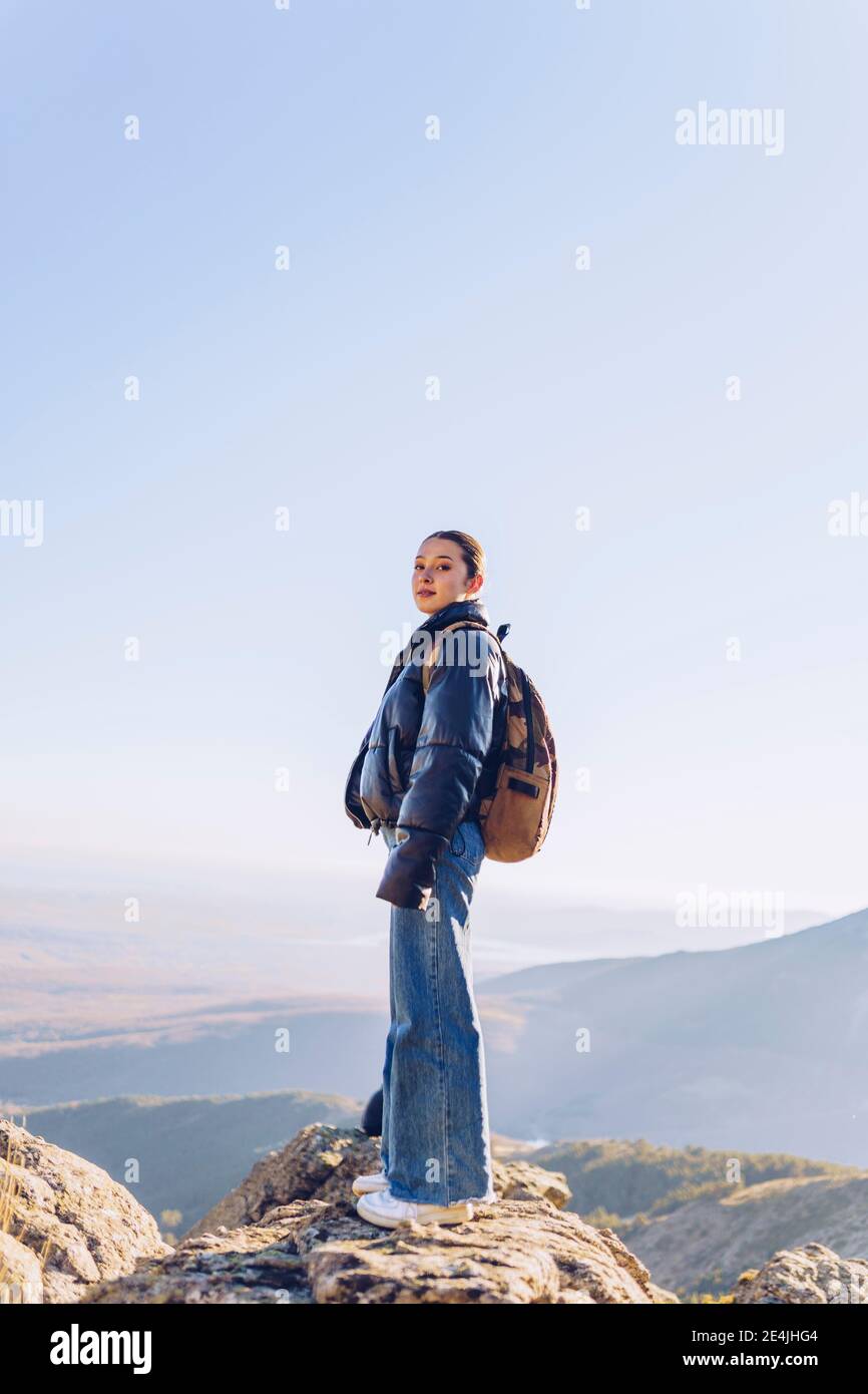 Female hiker with backpack standing on top of mountain against clear ...