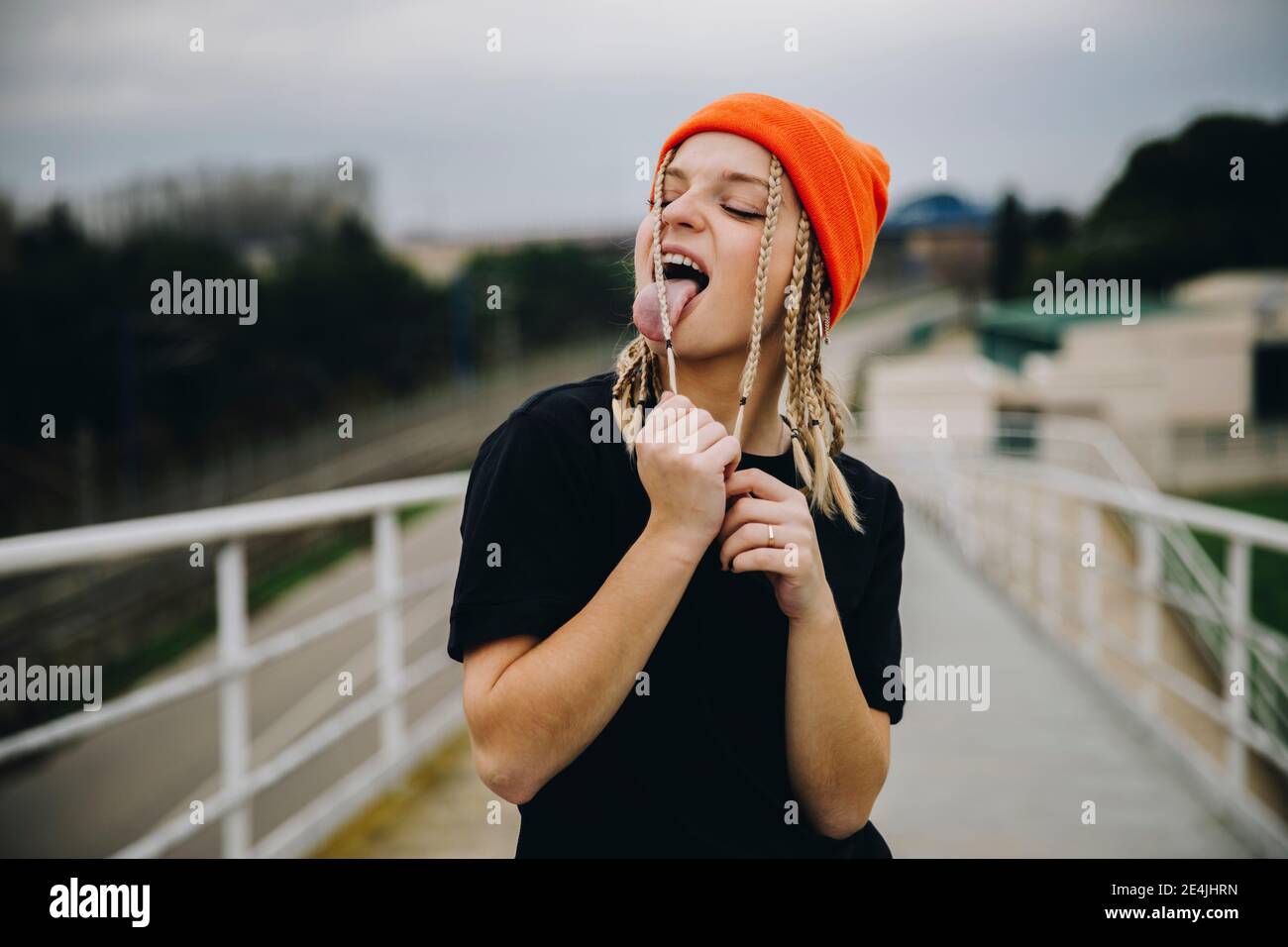 Young woman licking braided hair while standing on footbridge Stock Photo