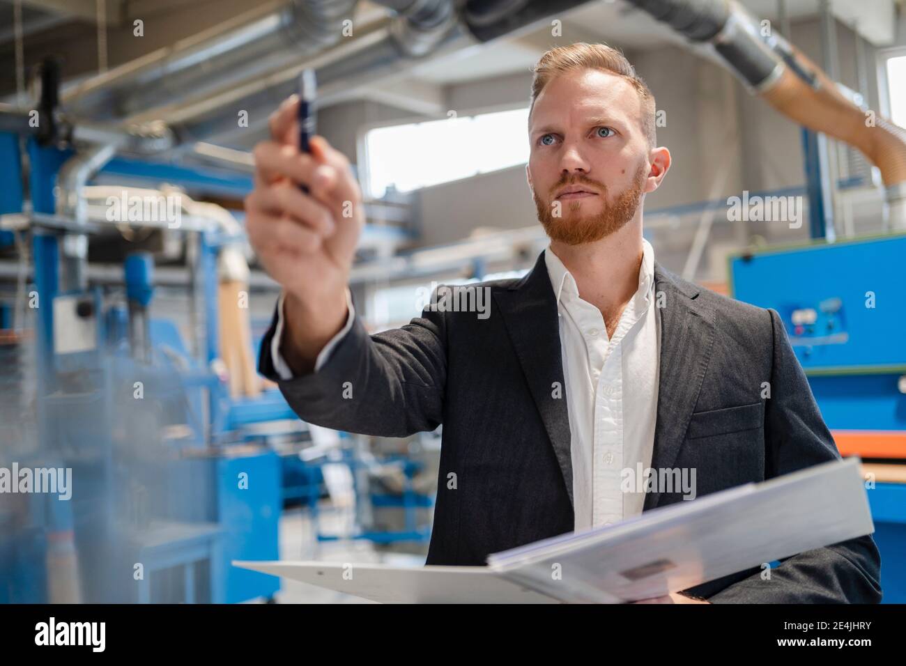 Portrait of well-dressed carpenter standing in production hall with ring binder in hands Stock Photo