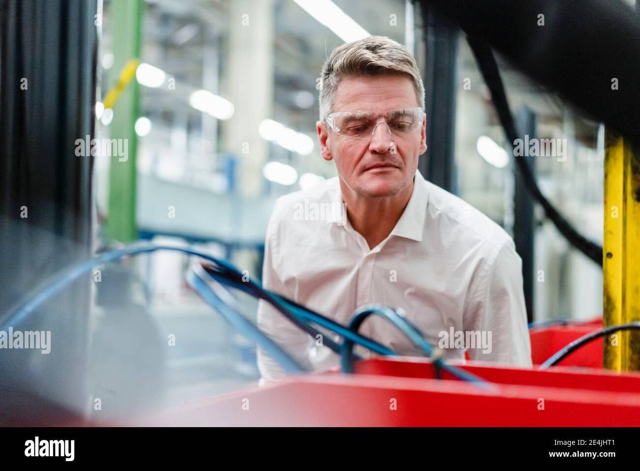Mature manager wearing protective eyewear examining machinery in industry Stock Photo