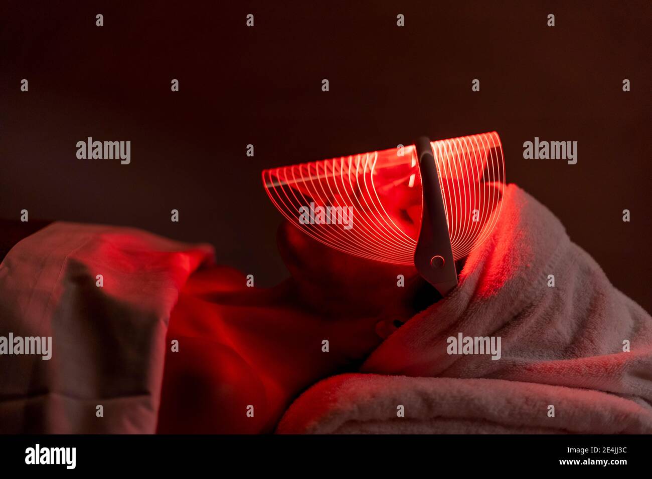 Young woman wearing red mask during rejuvenating treatment in dark at beauty spa Stock Photo