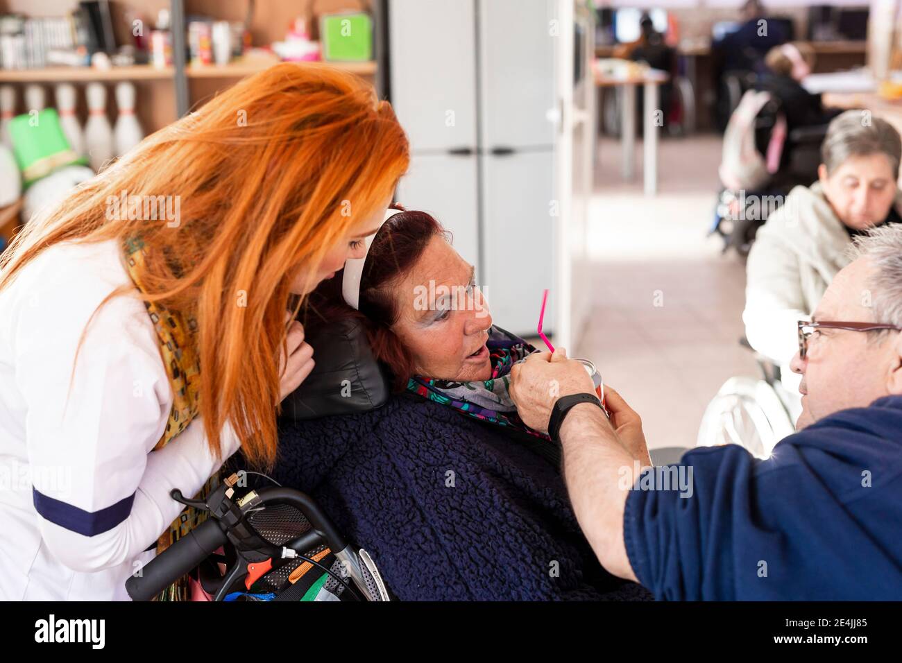 Female caregiver looking while mature man giving cold drink to disabled woman at rehabilitation center Stock Photo
