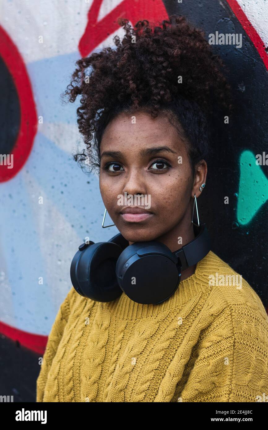 Confident young woman with curly hair wearing headphones against