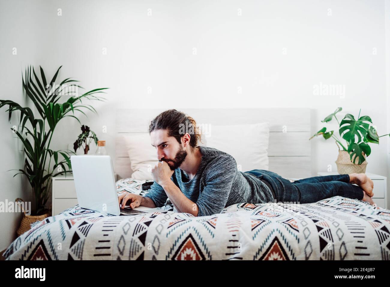 Young man working on laptop while lying on bed at home Stock Photo - Alamy