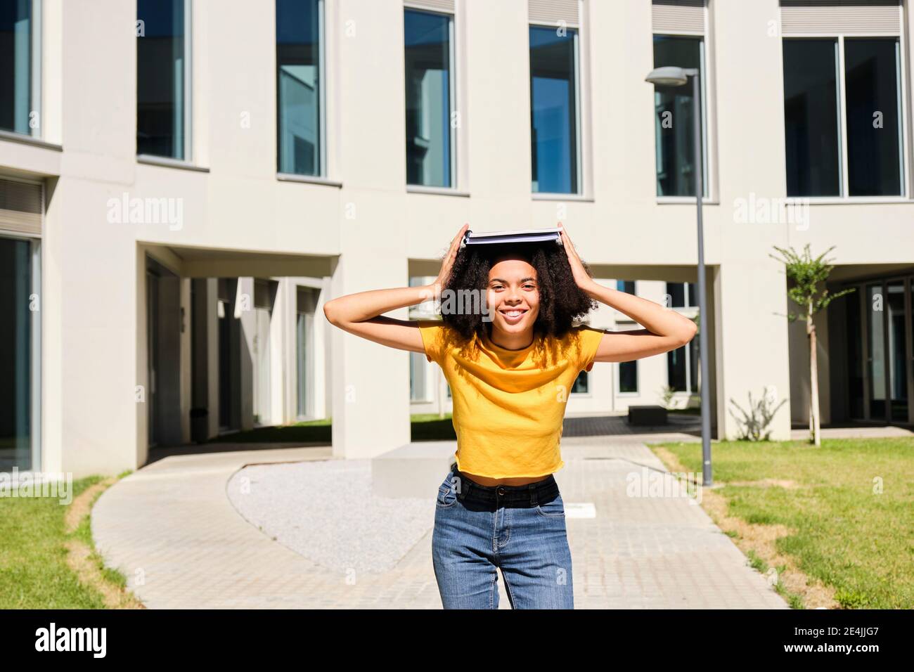 Smiling female student holding book while standing at university Stock Photo