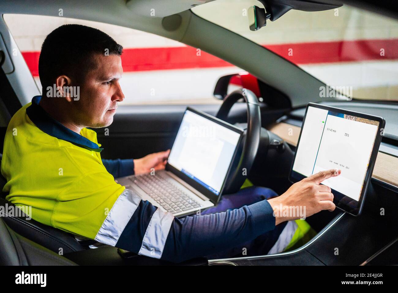 Male programmer with laptop working on digital tablet in electric car