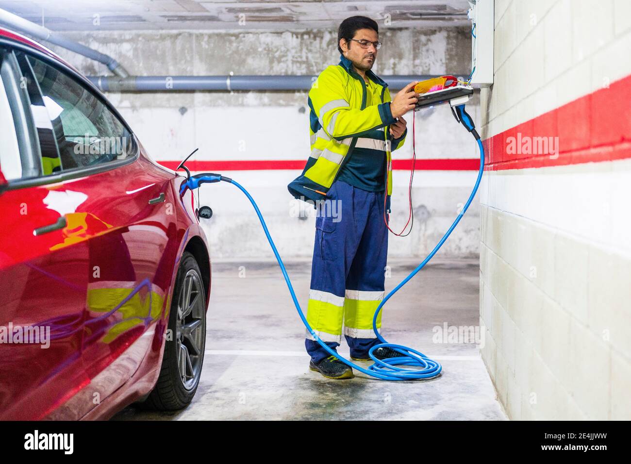 Male technician charging electric car at auto repair shop Stock Photo