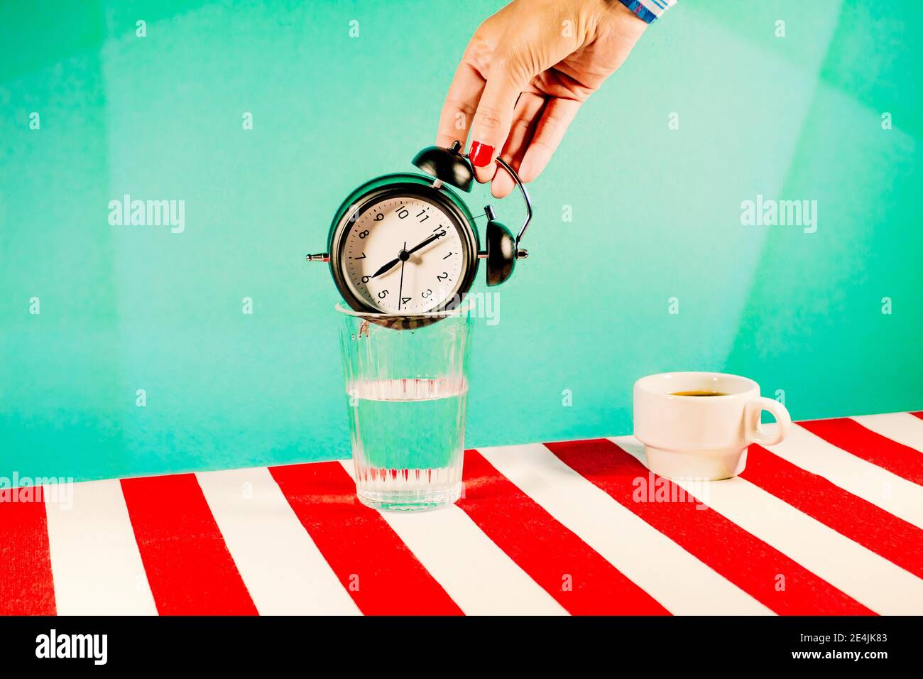 Hand of woman trying to put alarm clock inside glass of water Stock