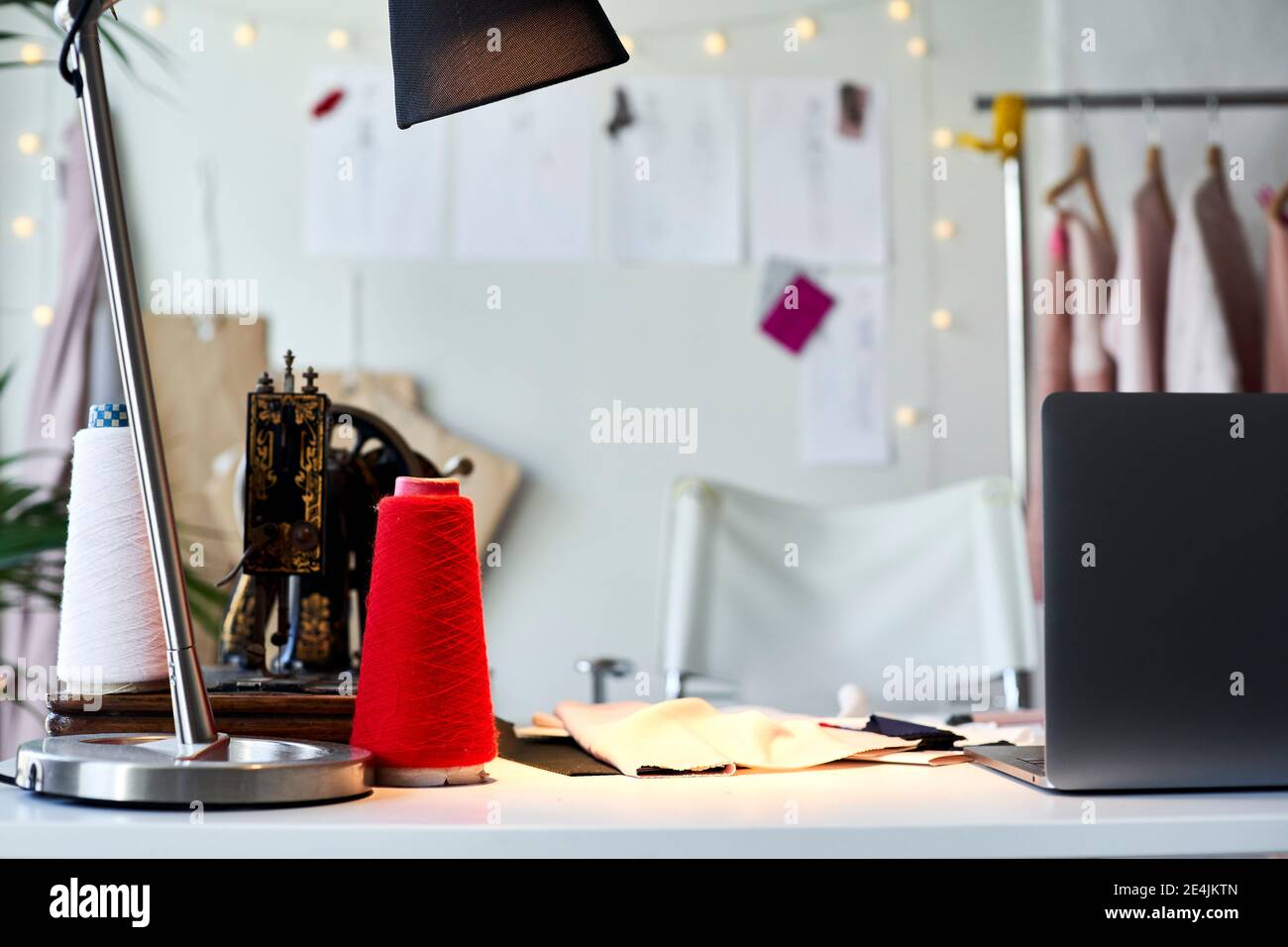 Thread spools and sewing machine with laptop on desk at design studio ...