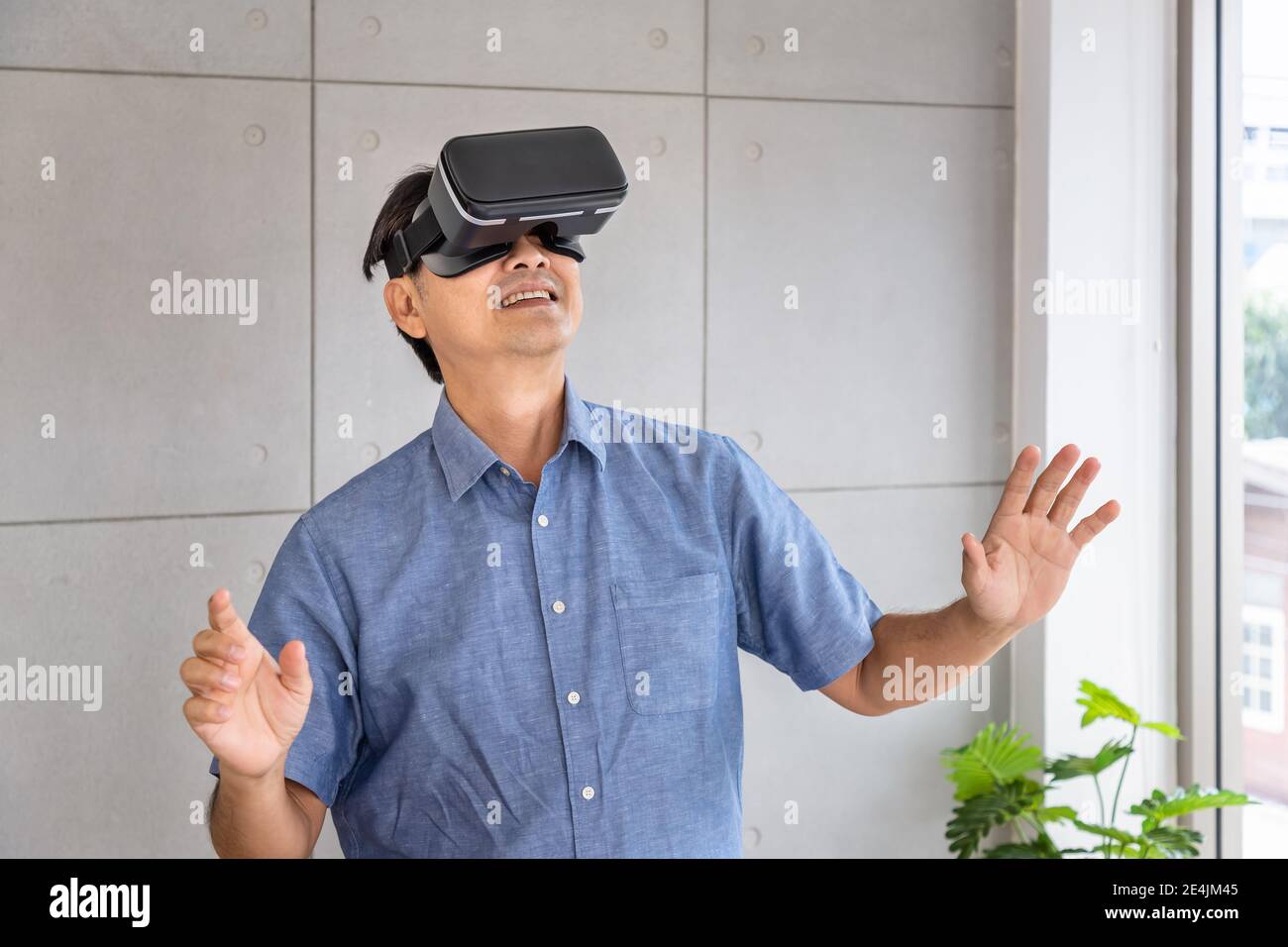 Senior retirement Asian man standing and wearing virtual reality glasses enjoy exciting experience Stock Photo