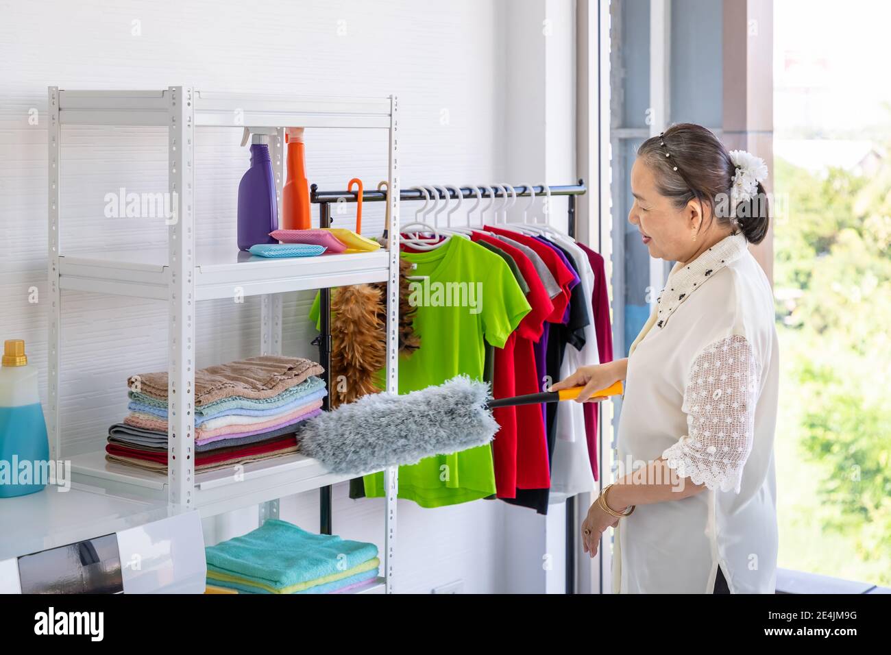 Asian senior elder woman clean shelf in laundry room using feather duster, spring cleaning concept Stock Photo