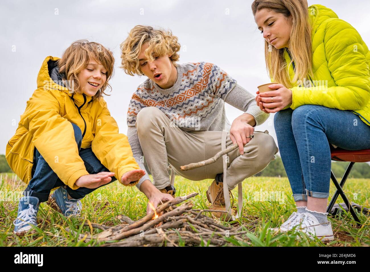 Three siblings starting campfire in grassy field Stock Photo