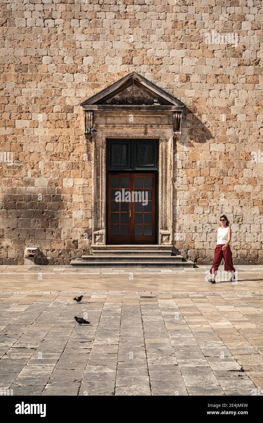 Croatia, Dubrovnik, Woman walking in front of old stone building Stock Photo