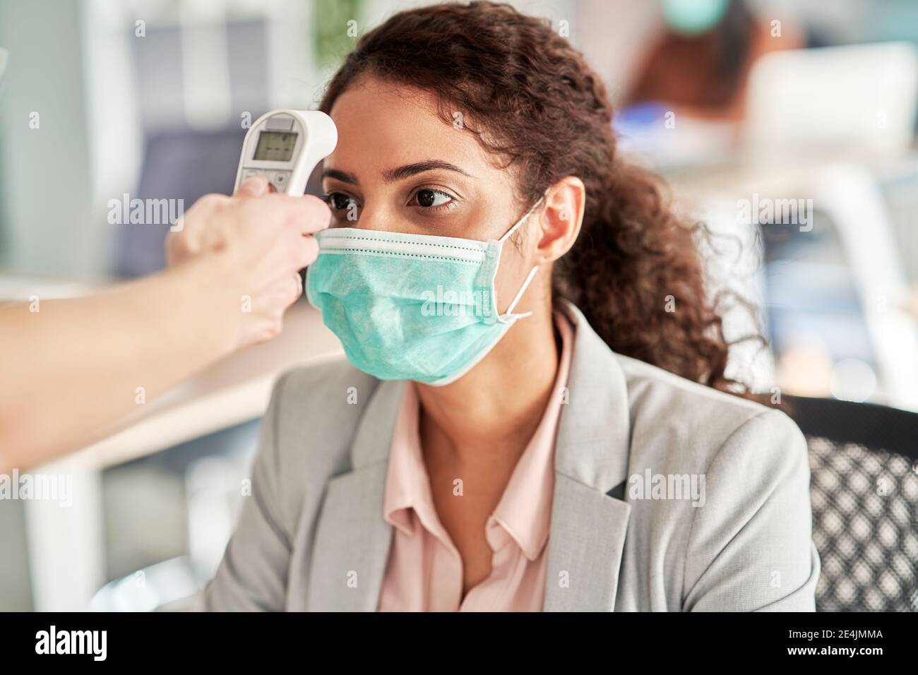Female professional going through thermometer checkpoint at work place Stock Photo