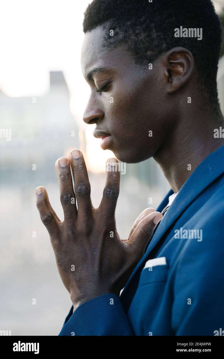 Young man with hands clasped and eyes closed standing outdoors Stock Photo