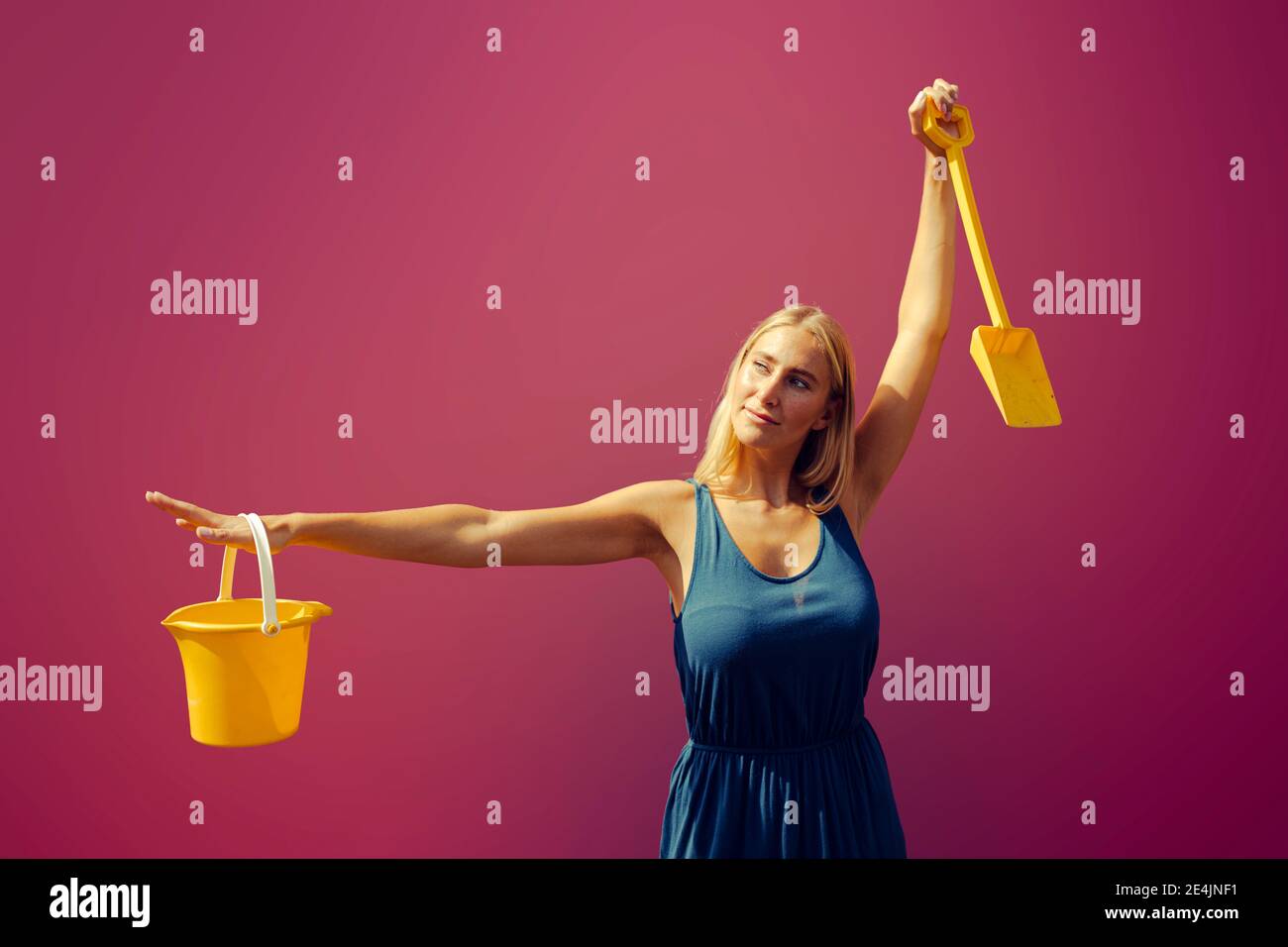 Young woman with sand bucket and shovel against purple Stock Photo