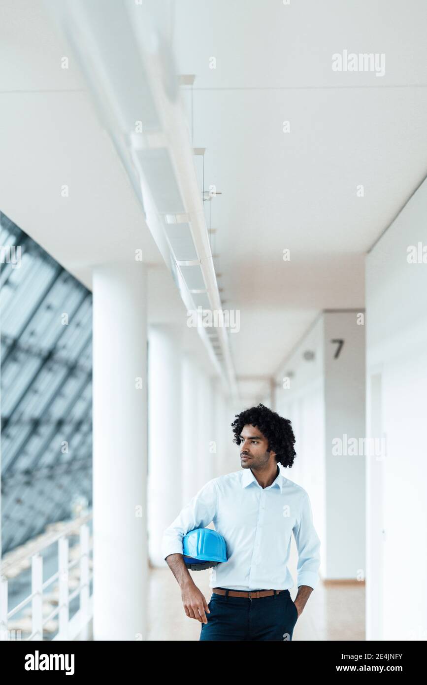 Young male engineer with hardhat looking away while standing in corridor at office Stock Photo