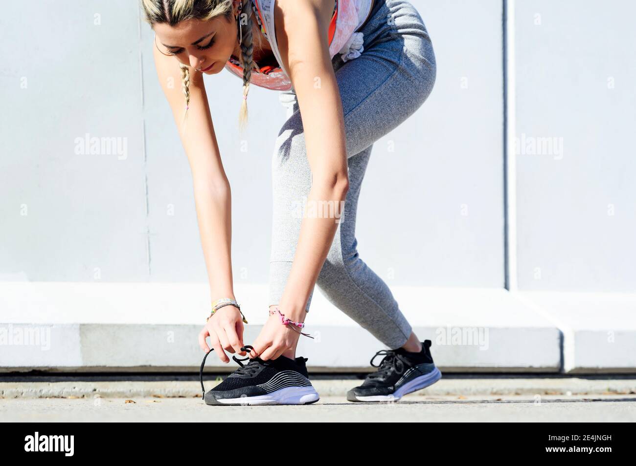 Sportswoman tying shoelace while standing on footpath Stock Photo