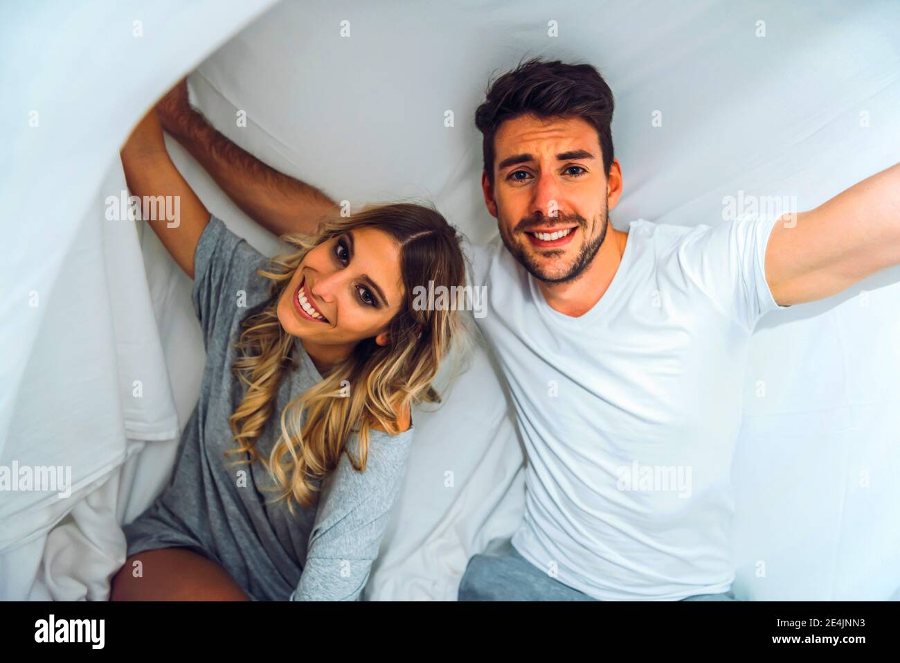 Portrait of happy young couple under sheets in bed Stock Photo