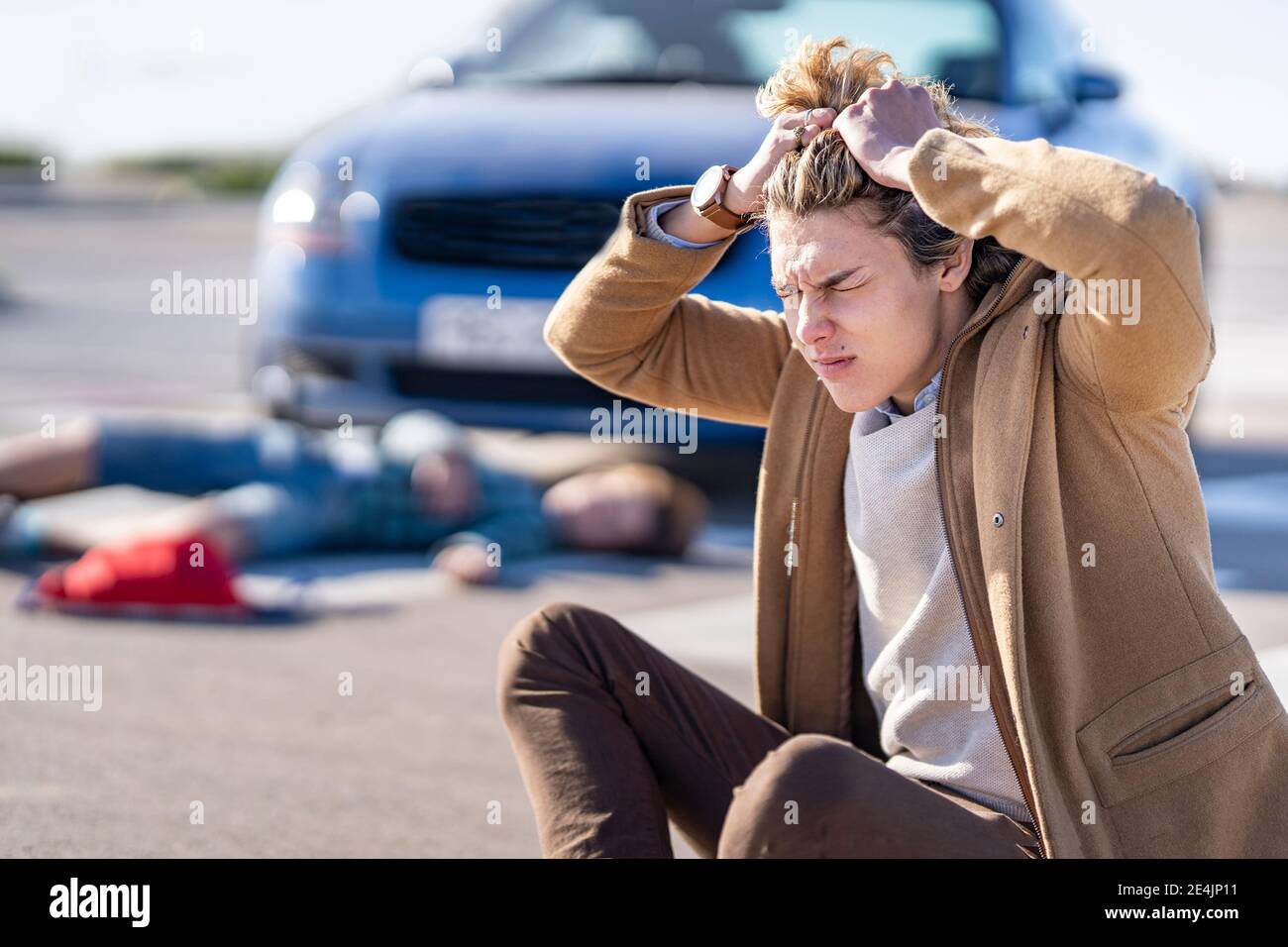 Desperate young man tearing his hair after car accident with boy lying on road in background Stock Photo