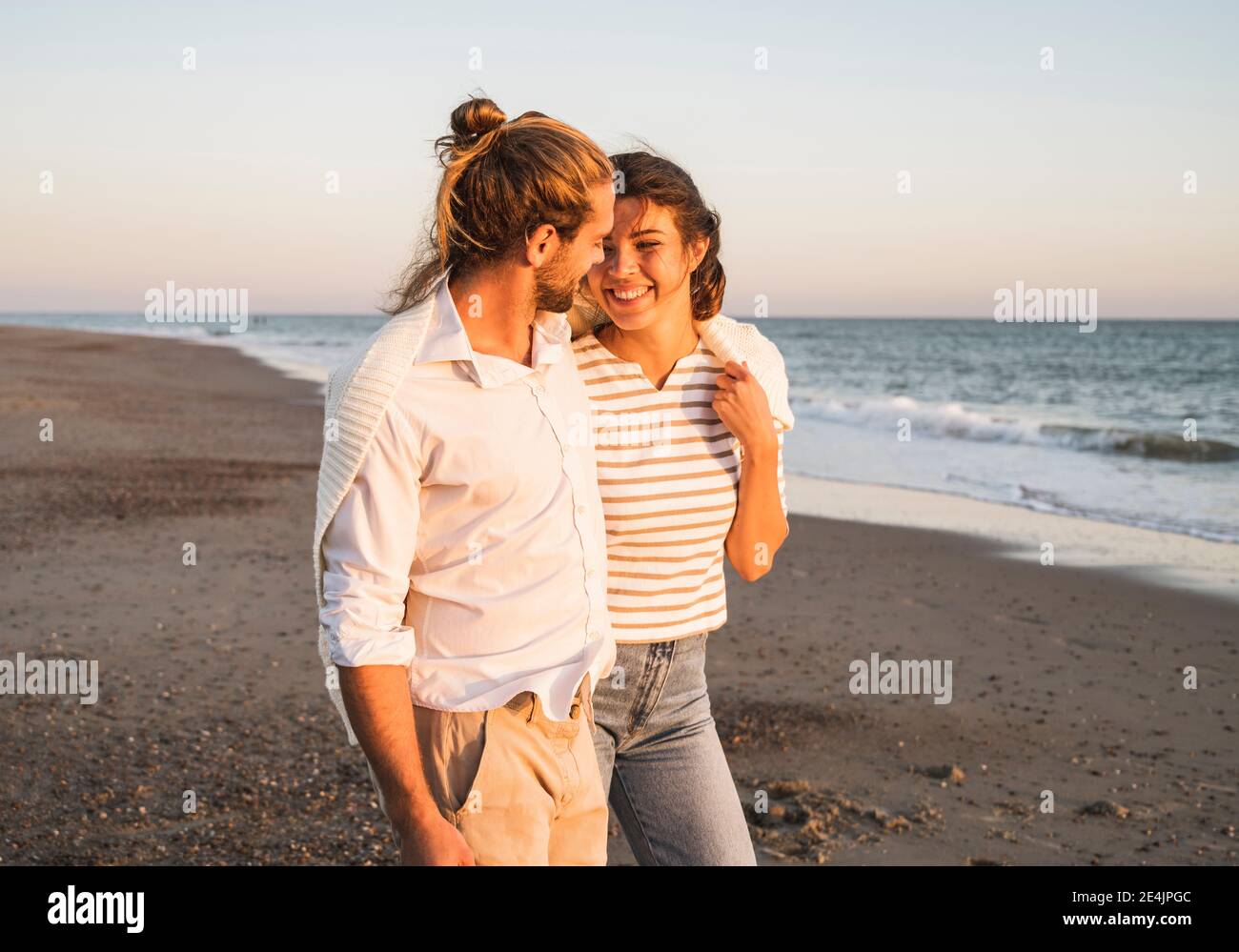 Smiling young woman walking with boyfriend at beach during sunset Stock ...