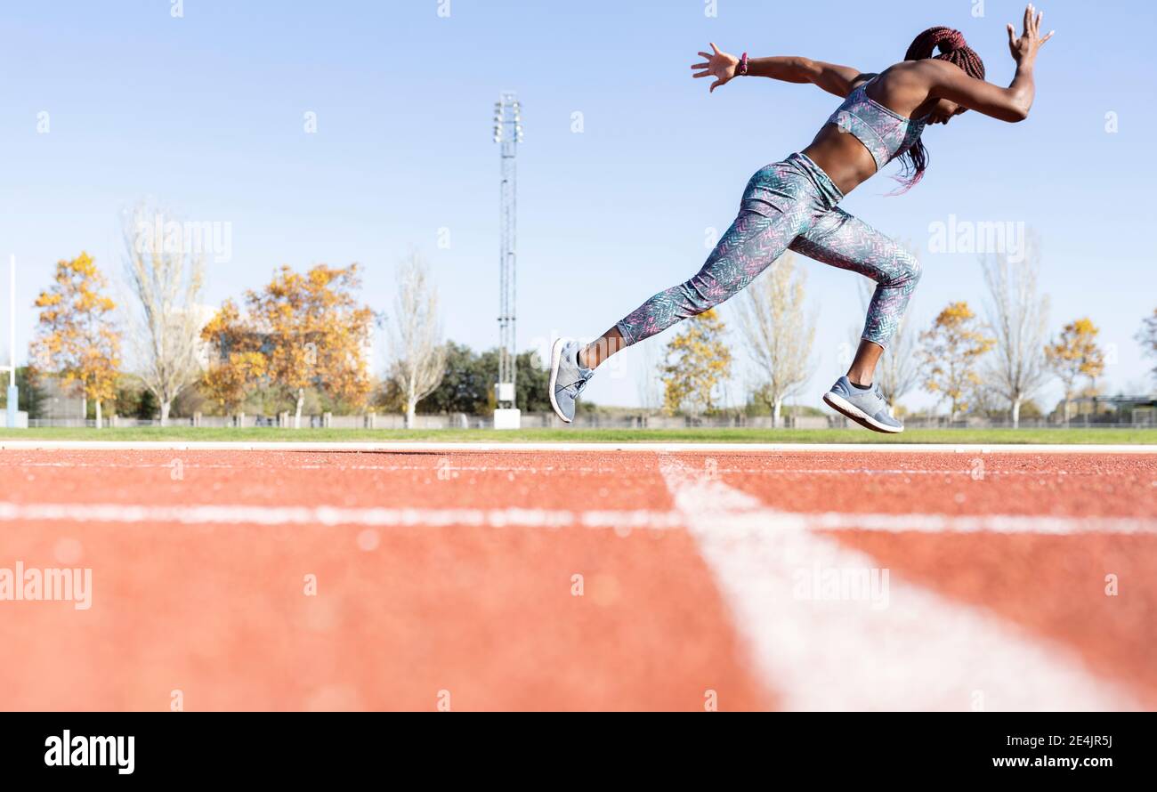 Sportswoman with dedication running on sports track against clear sky during sunny day Stock Photo