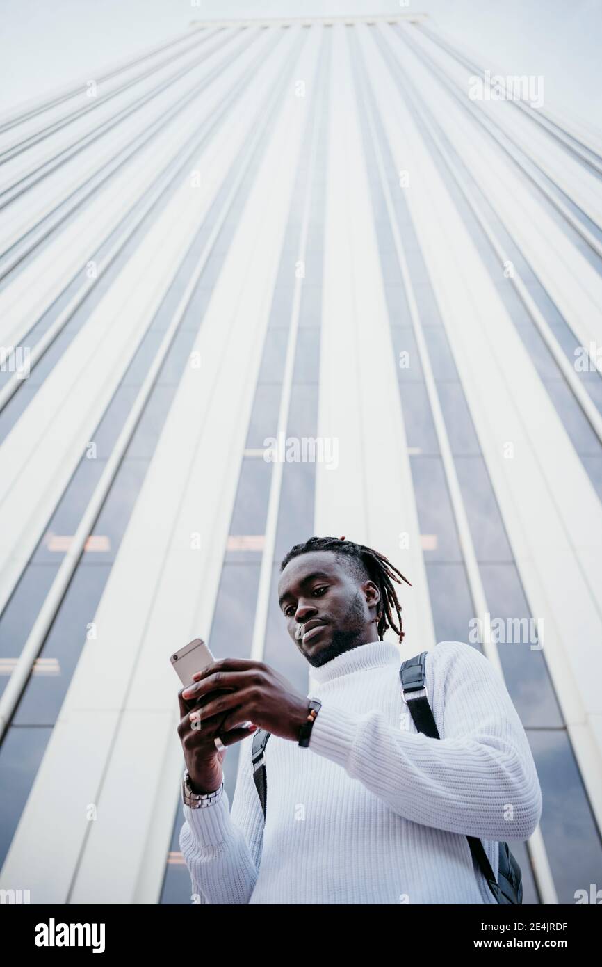 Young creative professional using smartphone against skyscraper in city Stock Photo