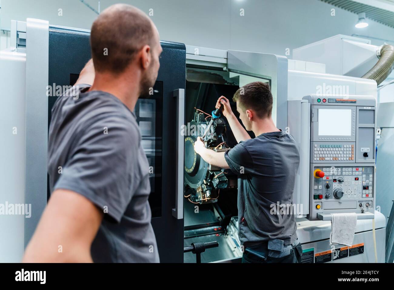 Trainee tightening bolts of machine while standing by instructor at industry Stock Photo
