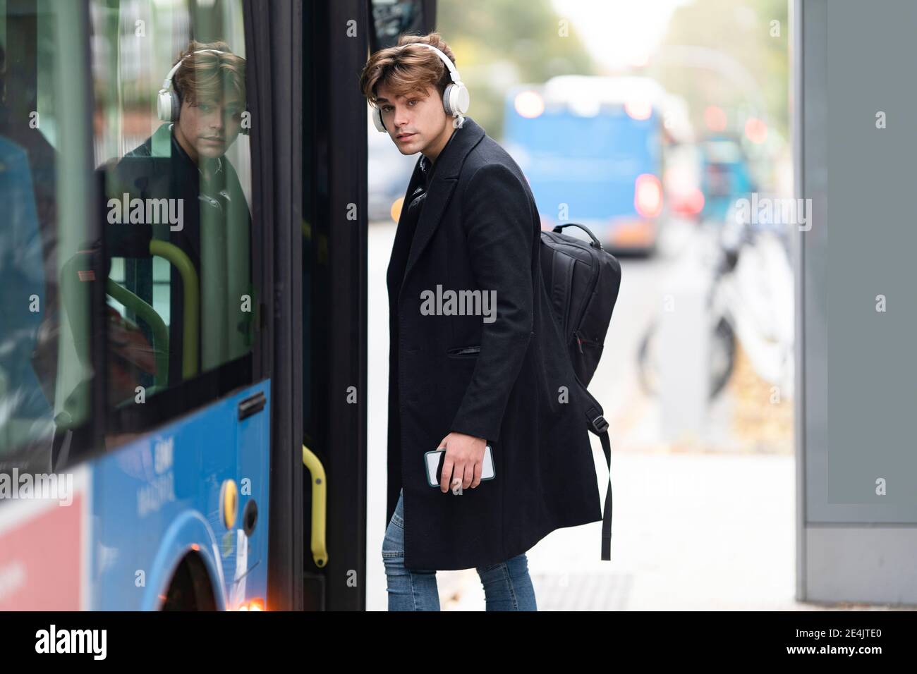Handsome young man with backpack listening music boarding bus in city Stock Photo
