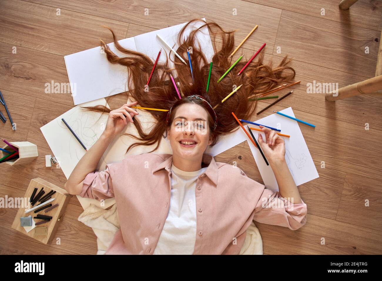 Smiling female artist with bunch of colored pencils in hair while lying