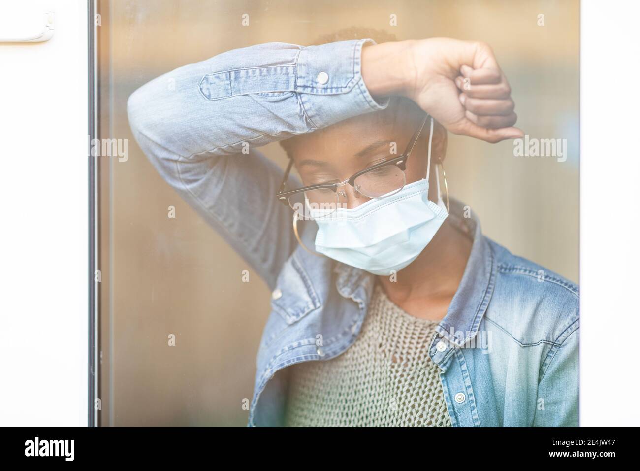 Sad woman in face mask leaning on window Stock Photo