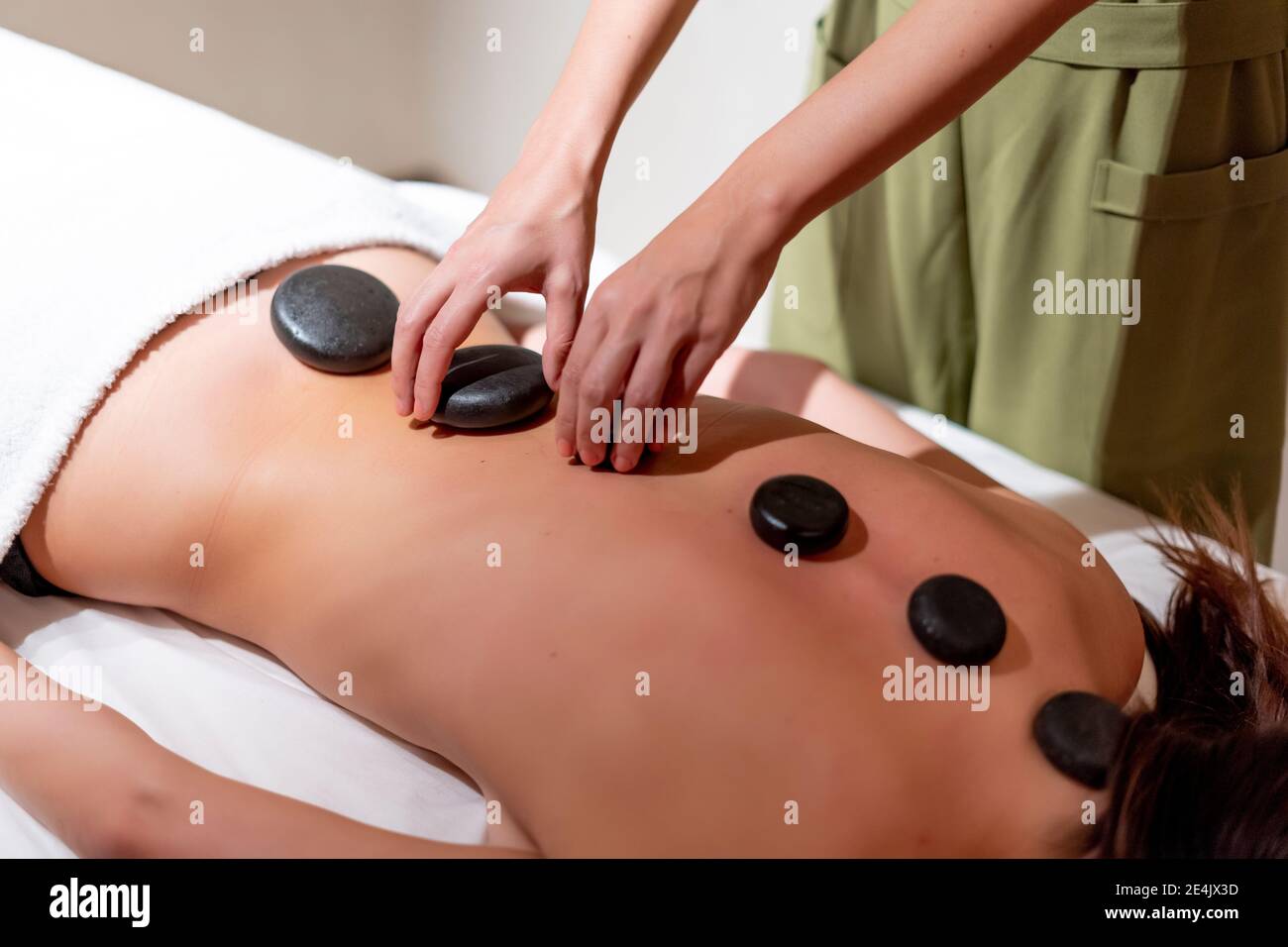 Mature massage therapist positioning stones on female customer's back at health spa Stock Photo