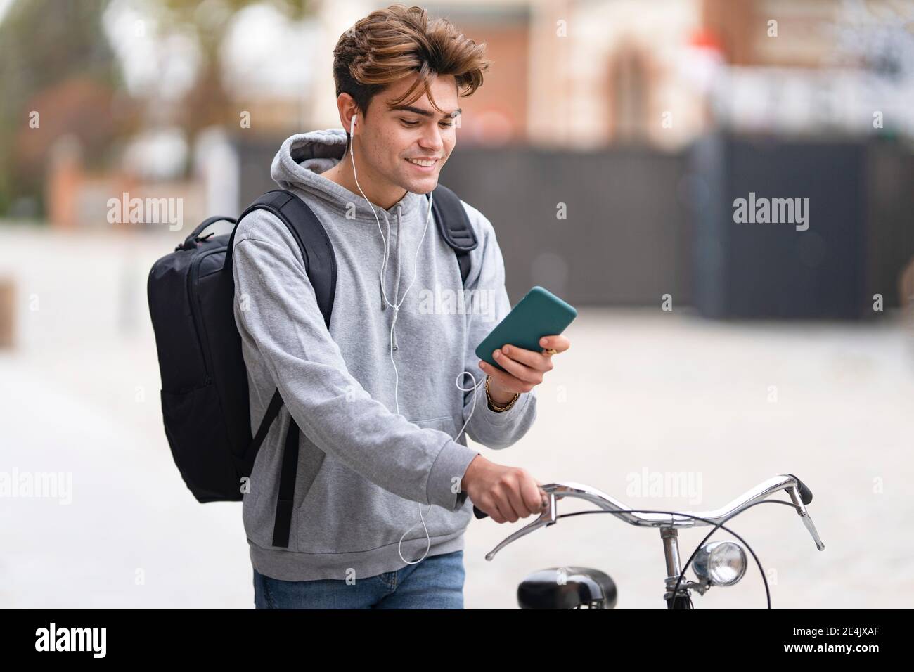 Smiling young man using mobile phone while wheeling bicycle in city Stock Photo
