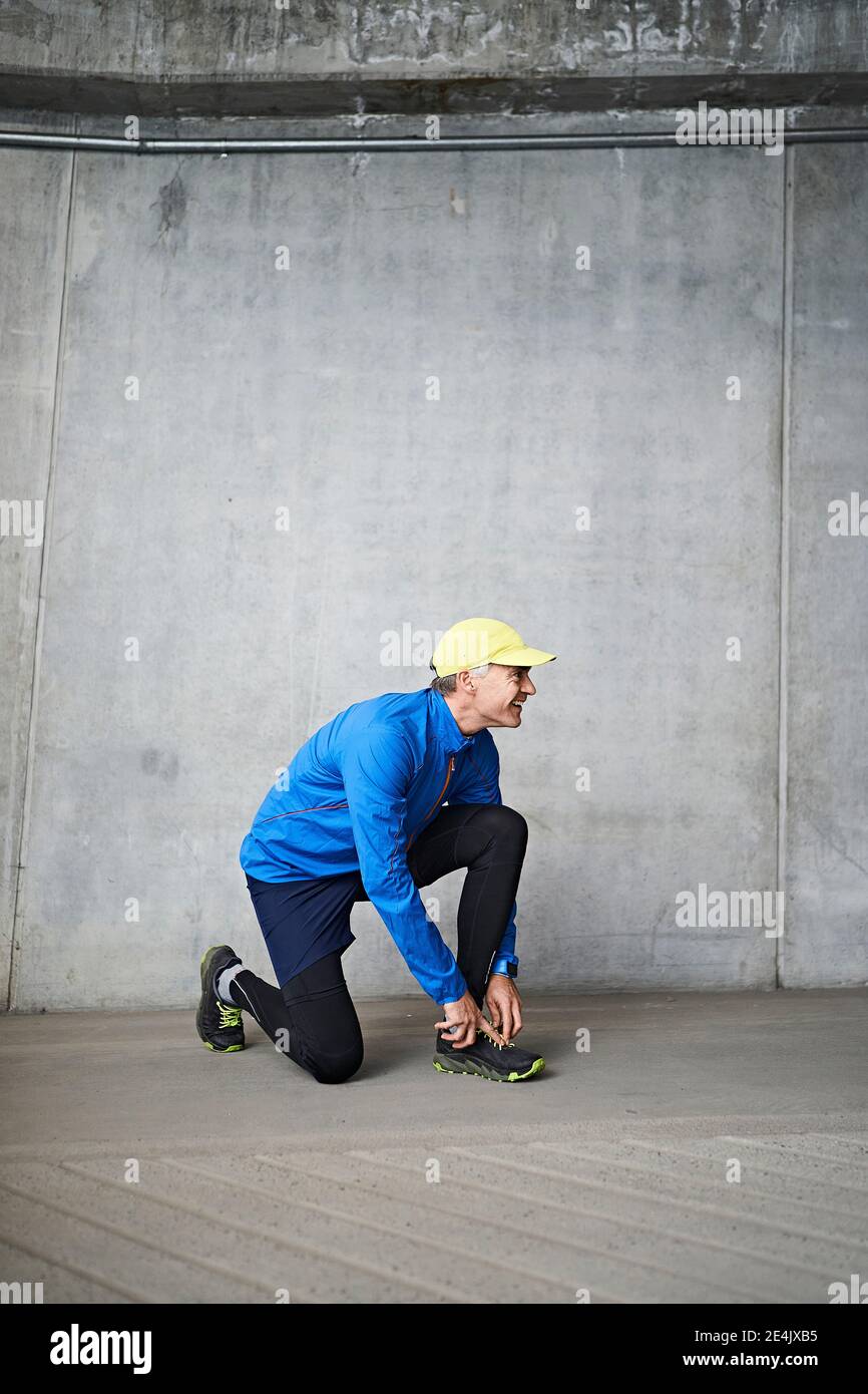 Mature man tying shoelace in parking garage against gray wall Stock Photo