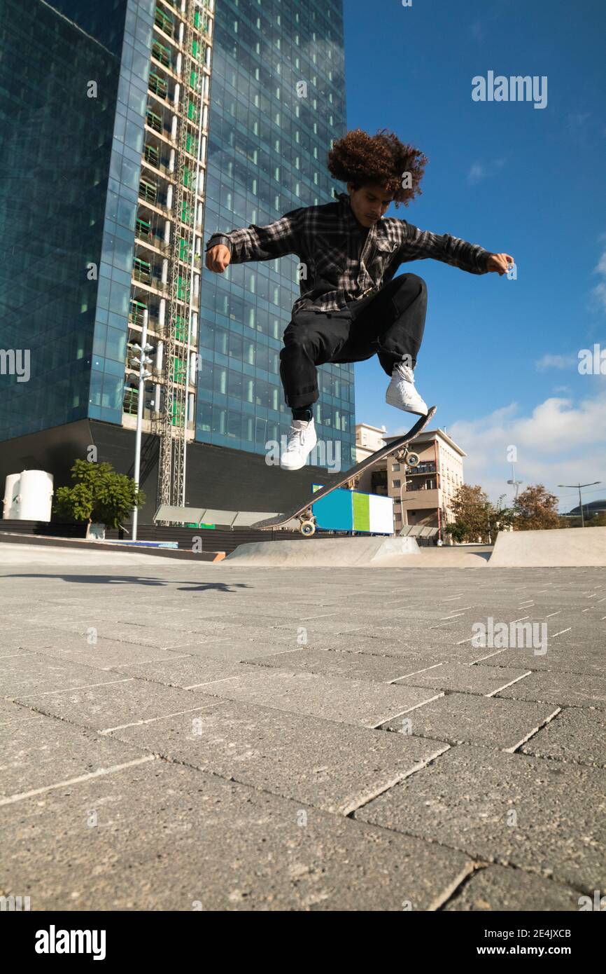 Curly hair sportsman practicing kickflip with skateboard at skateboard park Stock Photo