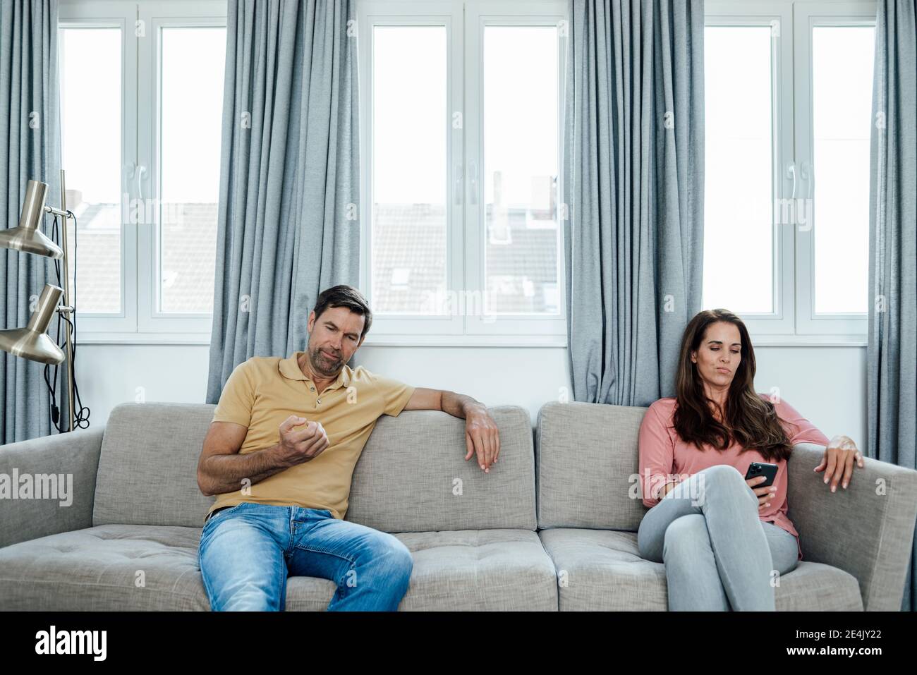 Mature woman using phone while man looking at nails at home Stock Photo