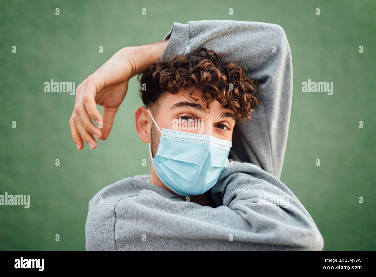 Man with hand raised wearing surgical mask against green background in ...
