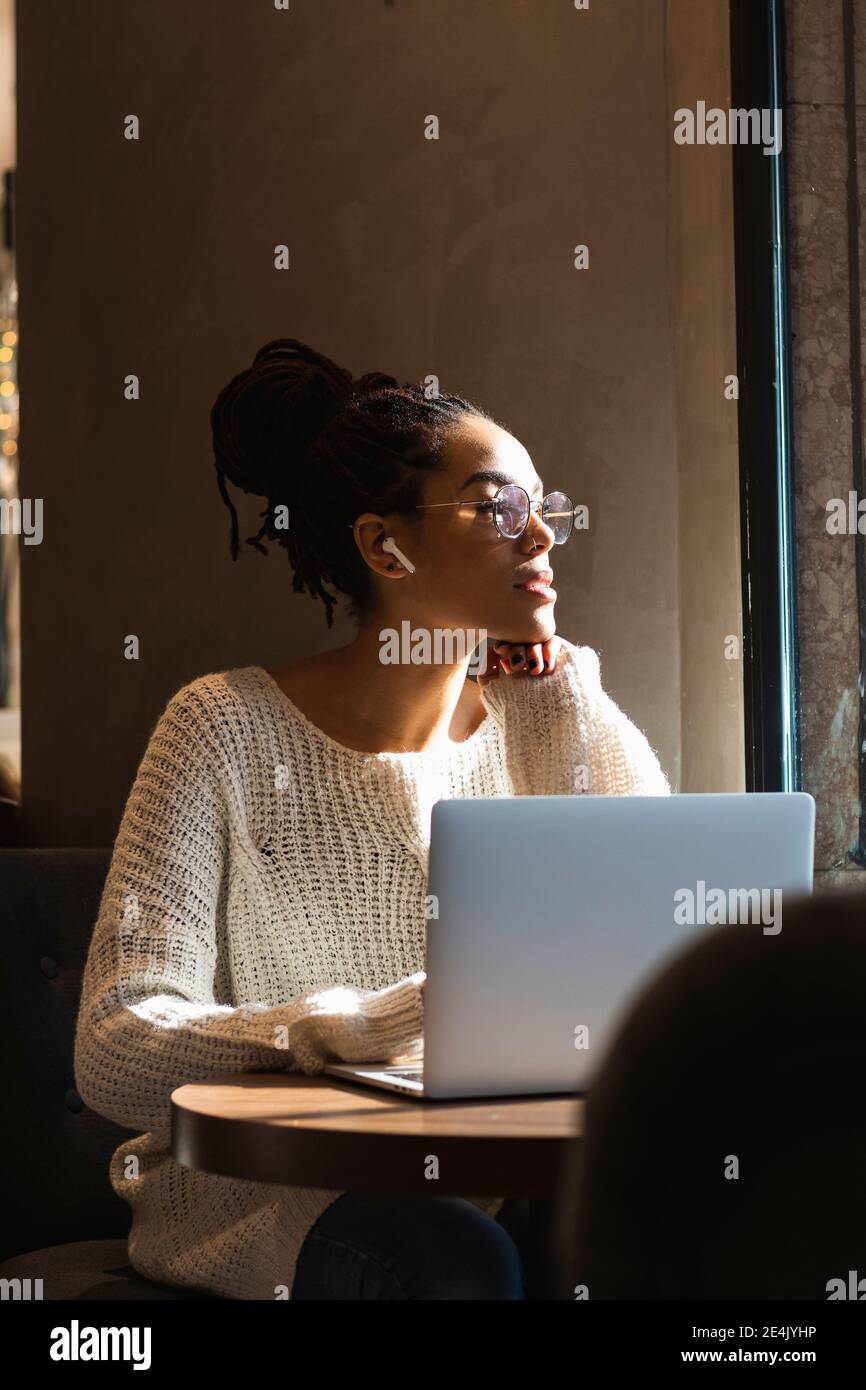 Young thoughtful woman looking away while sitting with laptop at cafe Stock Photo