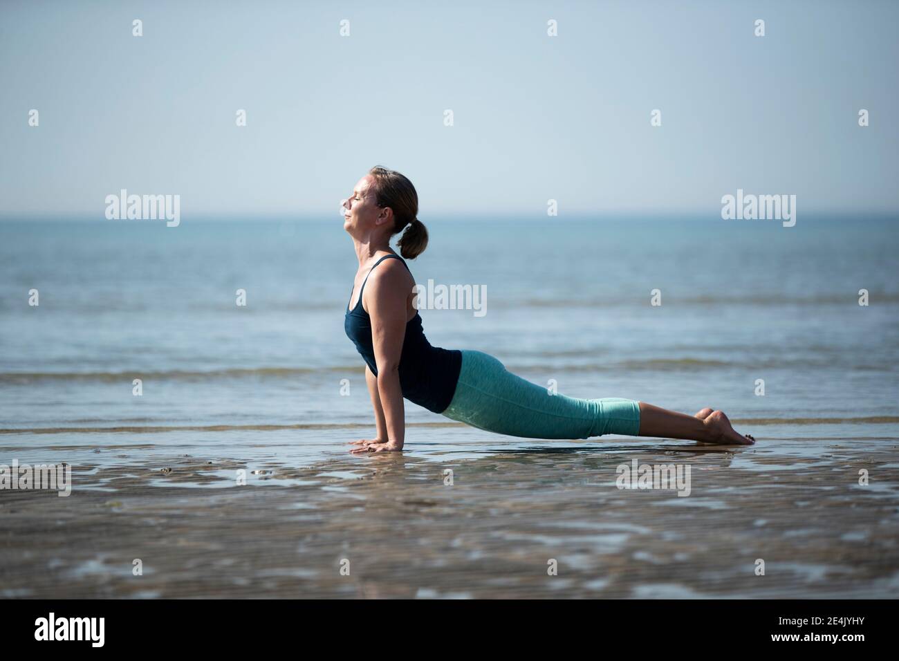 Mature woman practicing upward facing dog position at beach against clear sky Stock Photo